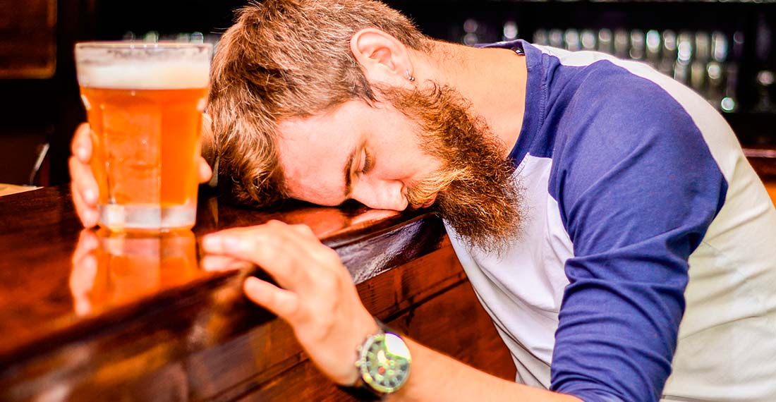 muž s hrnkem piva spí za barem